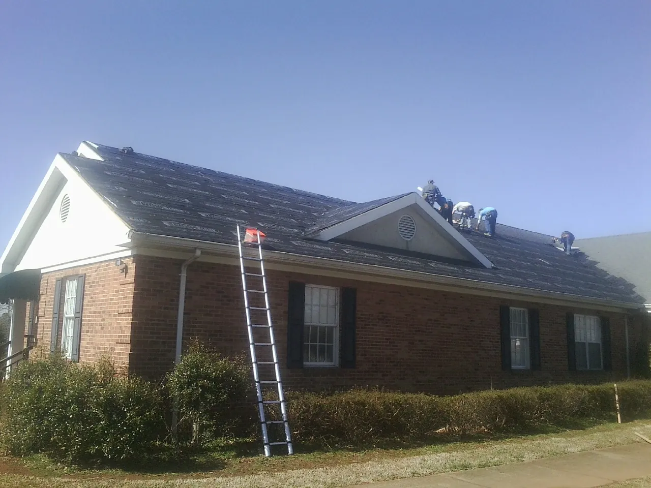 Crew tearing shingles off a brick ranch roof with a ladder set — Metal Roof Repair work by our crew in Greenfield