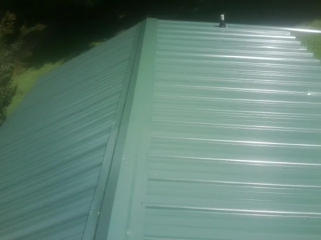 New green metal panels meeting at the ridge of a roof — Flat Roof Repair work by our crew in Greenfield